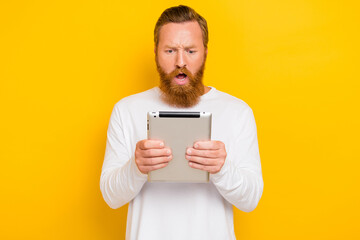 Photo portrait of handsome young man hold device tablet shocking comment wear stylish white pullover isolated on yellow color background