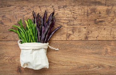 Green and purple string beans in woven bag on old wooden table