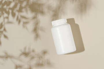 Vitamin medical bottle on beige background with leaves shadows, bio supplement, natural vitamins,...