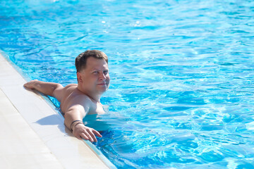 Adult rich man bathes in the blue water of the pool.