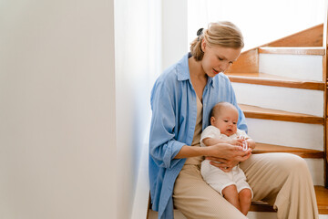 Young white mother wearing shirt holding her baby in arms at home