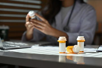 Fototapeta na wymiar Selective focus on pill bottles with empty label and female pharmacist checking pill bottles and reading drug labels as the background.