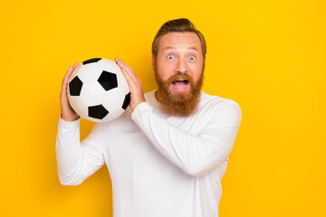 Portrait of overjoyed impressed man hands hold football open mouth isolated on yellow color background