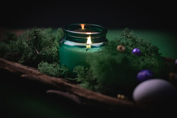 A burning candle in a glass jar in the bark of a tree with moss and precious ritual stones on a...