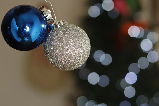 Primer Plano de par de esferas de navidad frente a un desenfoque de luces de navidad y árbol navideño