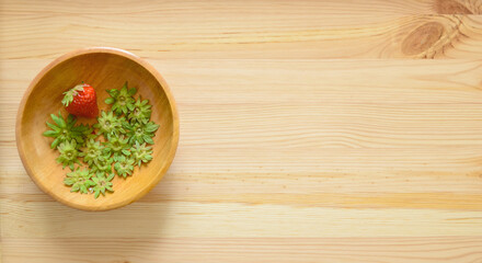 Top view of a fresh red strawberry with multiple calyxes in a wooden bowl on a wooden table.