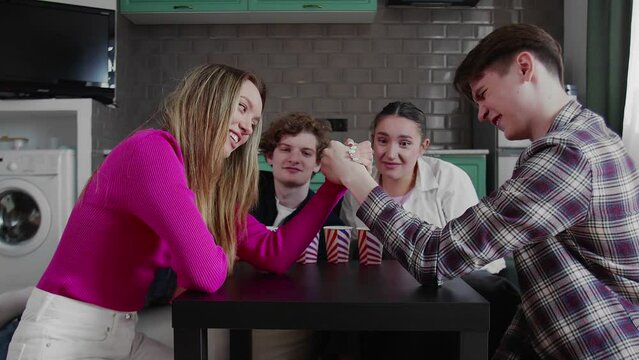 A group of friends are playing arm wrestling. Boy and girl wrestle on the table