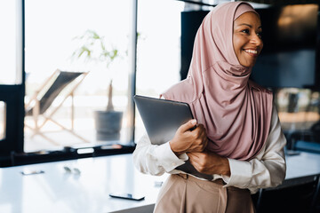 Happy muslim businesswoman holding clipboard while working in office