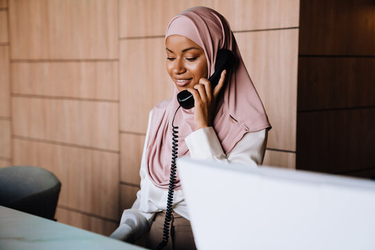 Muslim happy businesswoman talking on phone while working at reception