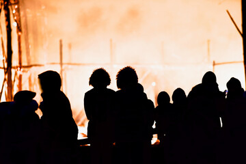 Dark silhouettes of people against the backdrop of a giant raging fire at night. The dark figures of a people against the backdrop of a burning building at night. People in front of the raging fire.