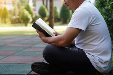Asian man is at the park, holds book to read. Concept : Relax time, pastime, hobby. Give time for yourself to read books , magazine, novels. Reading in daily life. Education ,knowledge or  pleasure. 