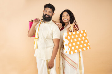 Happy South indian couple wearing traditional dress holding shopping bags and celebrating festival...