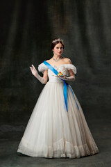 Fototapeta premium Young queen. Portrait of adorable girl in image of medieval royal person in renaissance style dress isolated on dark background. Comparison of eras, beauty, history, art