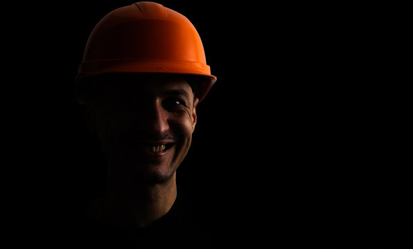 Dirty face of coal miner on a black background. Head of tired mine worker in a hard hat.