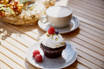 Aesthetic french berries cupcake with cappuccino among autumn decoration under sunny lights. Cozy breakfast at the terrace