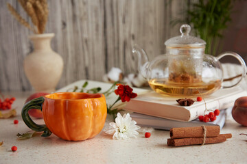 Herbal organic linden tea in teapot on the books and cup of tea in shape of pumpkin. Dry fragrant flowers, wheat, autumn arrangements, figs, peaches. Cozy atmosperic relaxing at home.