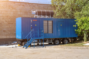 Modern blue diesel powered emergency backup electric generator on portable trailer. Industrial mobile diesel generator for office building, connected to electrical network by cable.