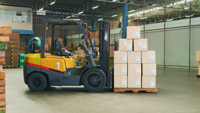 Side view of a forklift with stacked cargo cardboard boxes on wooden pallet in a large warehouse waiting for transportation by container trucks, ships, or planes. A lot of boxes with barcodes to tag a