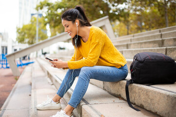 Fototapeta premium Side of smiling young woman sitting with cellphone listening to music