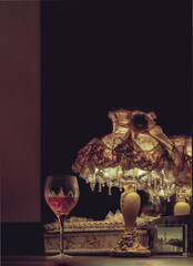 A glass of red wine puts on dressing table in the dim light of Vintage night lamp with reflection from mirror in the bedroom at night. Light and Shadow, Dark tone, Selective focus.