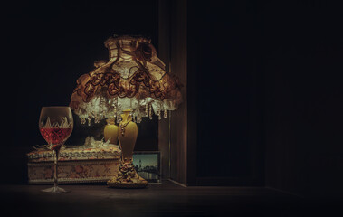A glass of red wine puts on dressing table in the dim light of Vintage night lamp with reflection...