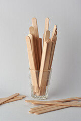 close-up of wooden ice cream sticks on a glass and scattered on neutral gray background