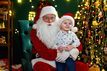 Fototapeta na wymiar Happy little boy sitting with Santa Claus near Christmas tree. New Year concept 