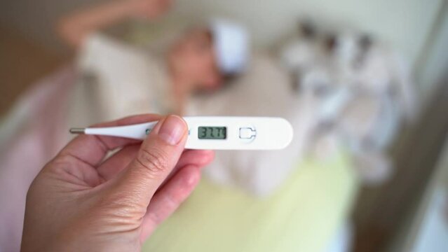Electronic thermometer with high temperature fever in mom hand. Mom measures body temperature of school child in bedroom at home. Cold and flu season.