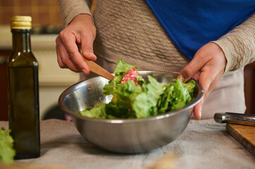 Details: woman's hand using wooden spoon, mixes fresh ingredients, lettuces leaves and organic vegetables, cooking salad. Healthy eating. Food concept. Slimming. Dieting. Weight loss and vegetarianism