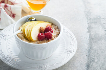 Oatmeal. Bowl of oatmeal porridge with raspberry, pear and honey on gray concrete old table background. Hot and healthy food for Breakfast, top view, flat lay