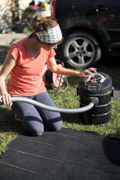Serene Caucasian Woman Cleaning Carpet from Her Car with a Vacuum Cleaner  in the Home front yard