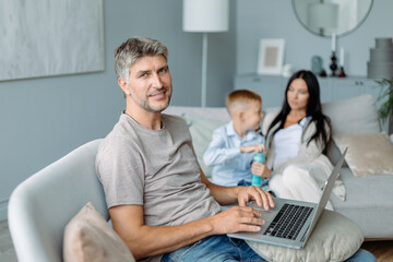 smiling father with a laptop sitting in a cozy living room.