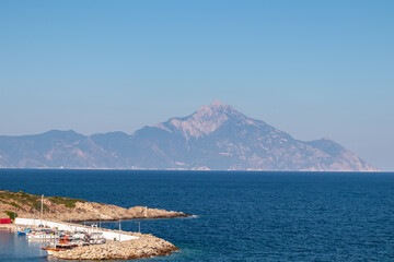 Scenic morning view of holy Mount Athos seen from small harbour port Sarti on peninsula Sithonia, Chalkidiki (Halkidiki), Greece, Europe. Summer vacation at Aegean Mediterranean Sea. Fishermen boats