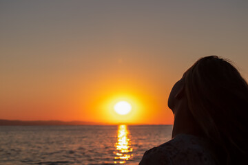 Fototapeta premium Silhouette of tourist woman holding the sun with panoramic view of sunset over Aegean Mediterranean Sea on Karydi beach, peninsula Sithonia, Chalkidiki (Halkidiki), Greece, Europe. Romantic atmosphere