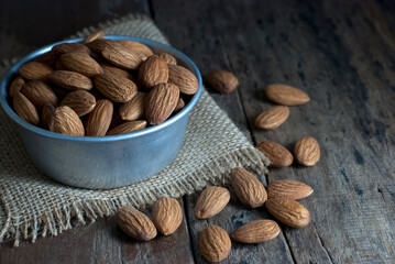 On a rustic wooden floor, almonds in a tin cup are placed on a sackcloth.
