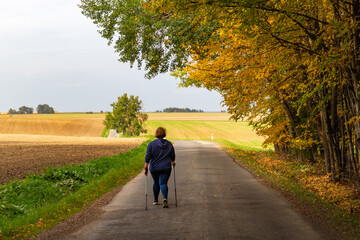 Fototapeta premium Plus size woman walking on the road. Nordic walking as healthy lifestyle and weight loss concept.