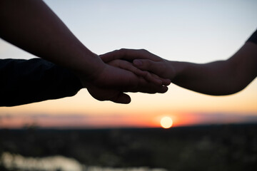 People's hands are stacked on top of each other for team development and team building against the background of the sunset sky. The concept of unity, mutual support and mutual assistance.