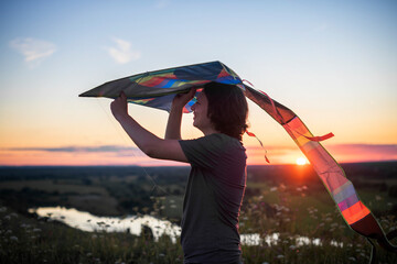 A teenager launches a kite at sunset in the summer in a field. The concept of hobbies, recreation and entertainment.