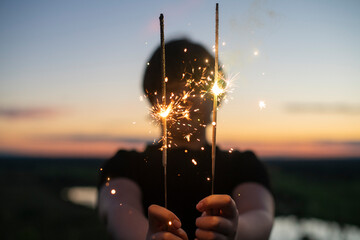 A cute boy holds sparklers in his hands, fireworks in the evening in the summer at sunset. Focus on the sparklers.