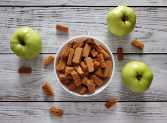 Apple croutons in white bowl, scattered apples on light wooden background, top view.