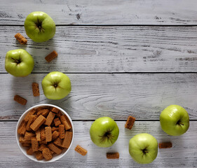 Apple croutons in white bowl, scattered apples on light wooden background, top view, flat lay.
