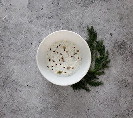 Sour cream sauce with garlic, dill and seeds in white bowl on light background, flat lay. 
