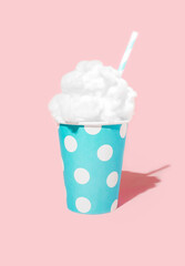 blue paper glass whit white dot and straw fulfilled with cloud whipped cream on bright pastel pink background. minimal creative composition.