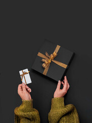 Black Friday Concept. top view photo of hands holding Black gift box with golden ribbon bow and...
