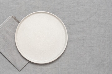 Empty beige plate mockup with gray linen napkin on gray linen background. Top view, flat lay, copy...