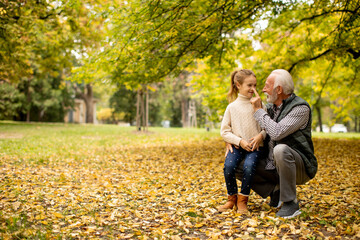 Fototapeta premium Grandfather spending time with his granddaughter in park on autumn day