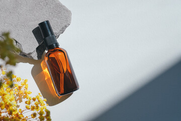 Amber pump bottle with serum, tonic or essential oil on grey concrete podium with yellow flowers....