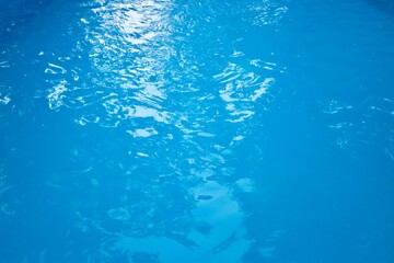 Fototapeta na wymiar Reflection of bright light in clean blue water of an outdoor swimming pool, small waves on surface