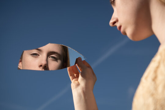 eyes of woman visible in reflection of broken mirror piece held by her hand