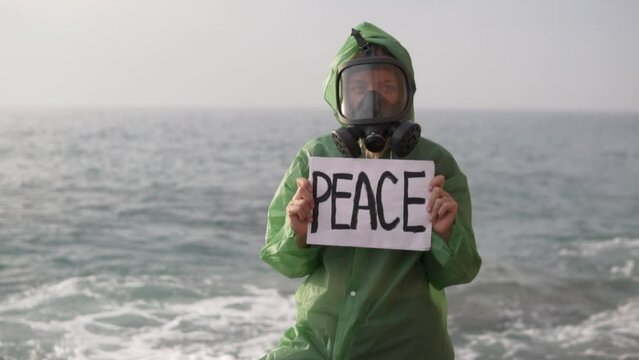 Close-up, woman in gas mask with poster - peace stands by the sea